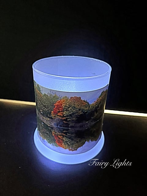 Glowing LED candle featuring autumn landscape with trees and water reflection on dark background