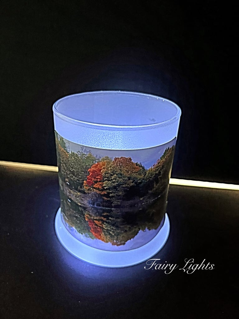 LED light-up cylinder with scenic autumn forest and water reflection image, glowing blue base on dark background